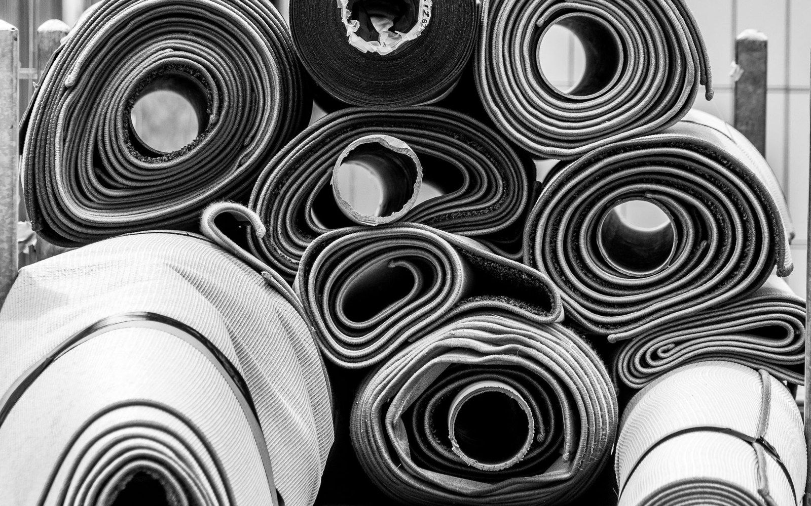 A warehouse wall stacked floor-to-ceiling with fabric rolls in neutral and primary colours, a worker visible in the left foreground