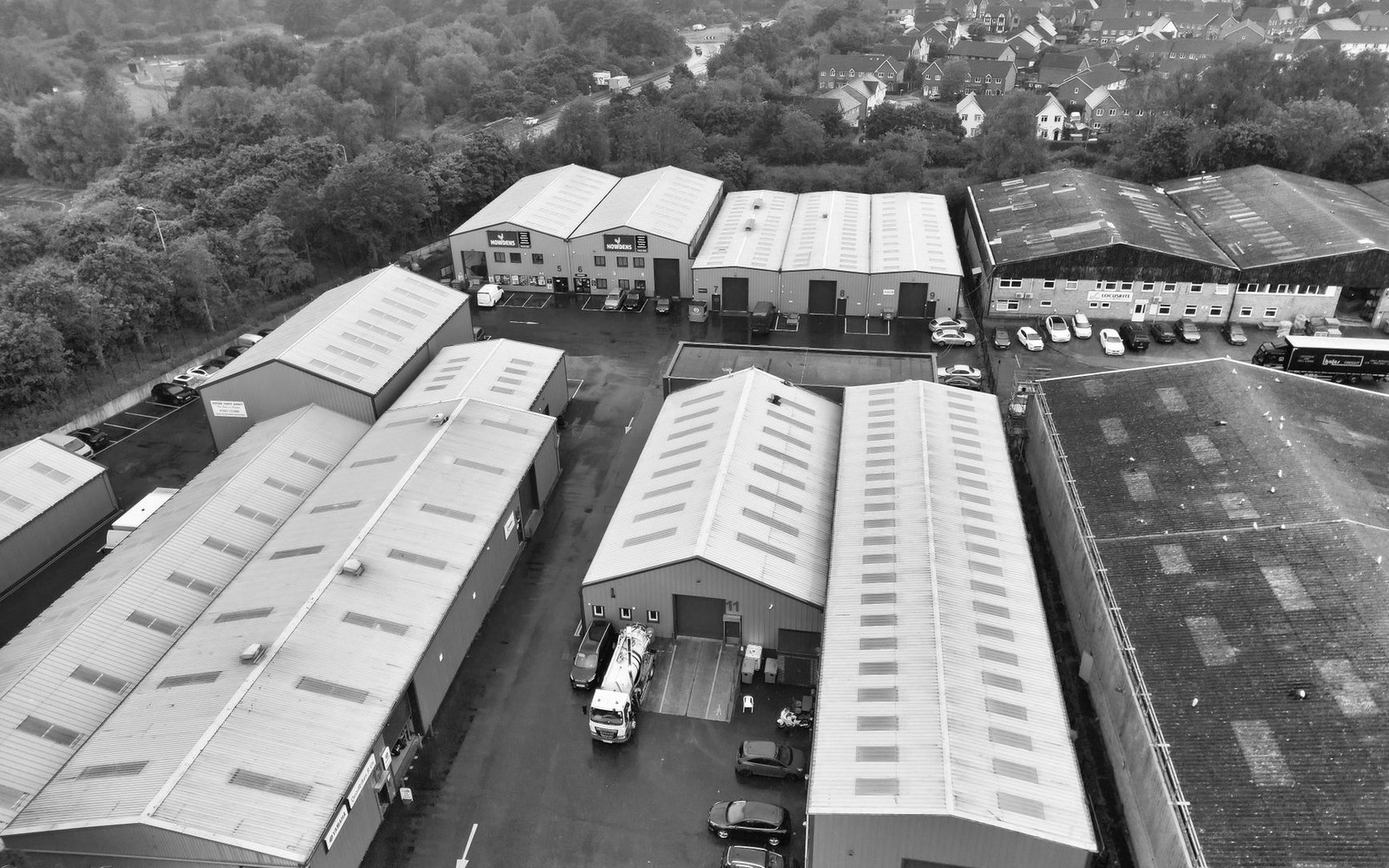 Aerial view of an industrial estate with warehouse units, parked vehicles and housing beyond