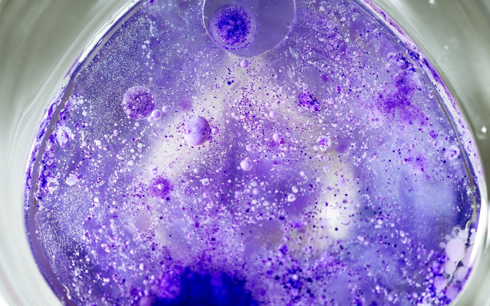 Purple dye dispersing and swirling with bubbles in a liquid solution