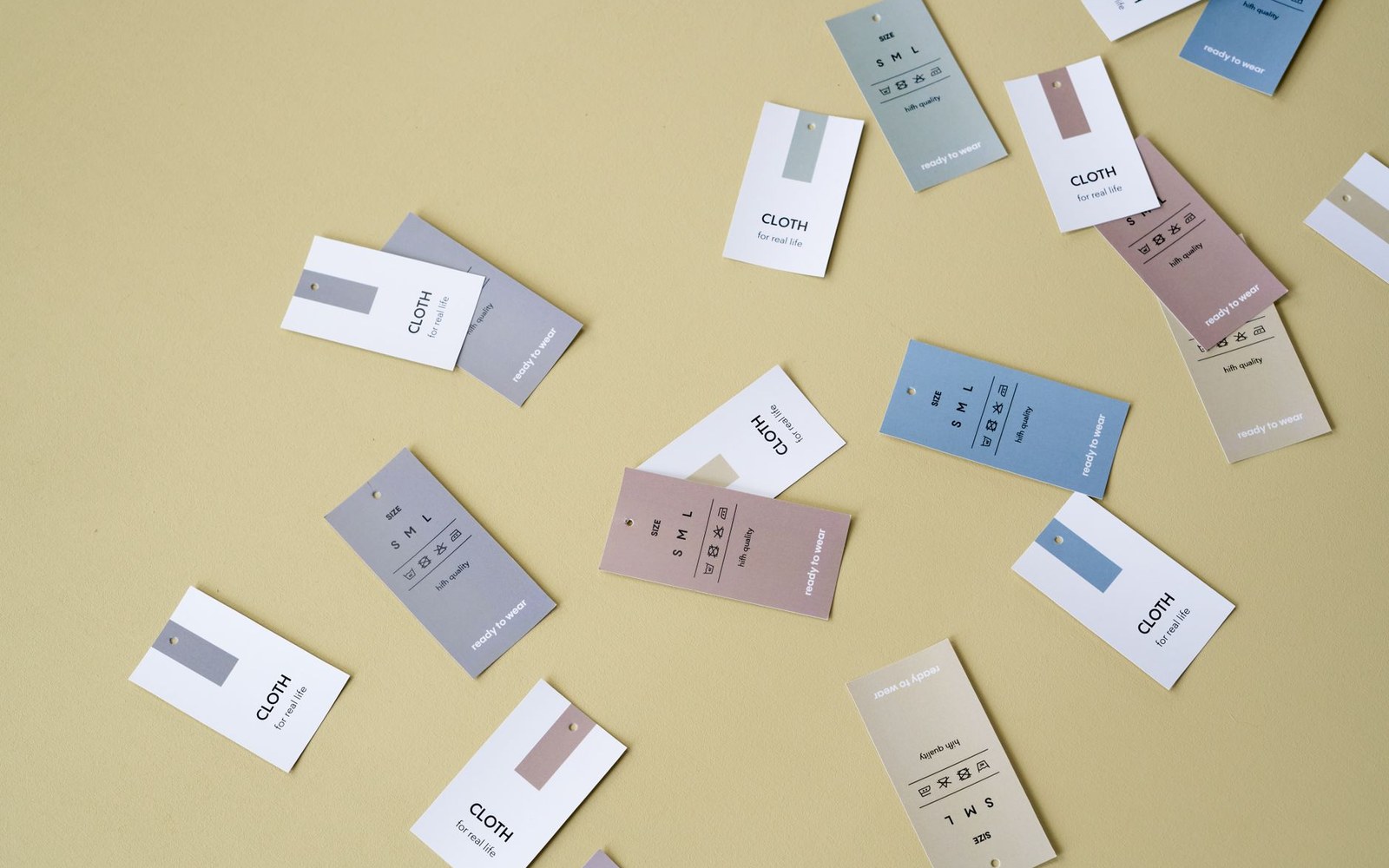 Scattered clothing size and care tags labeled Cloth for real life on a beige surface