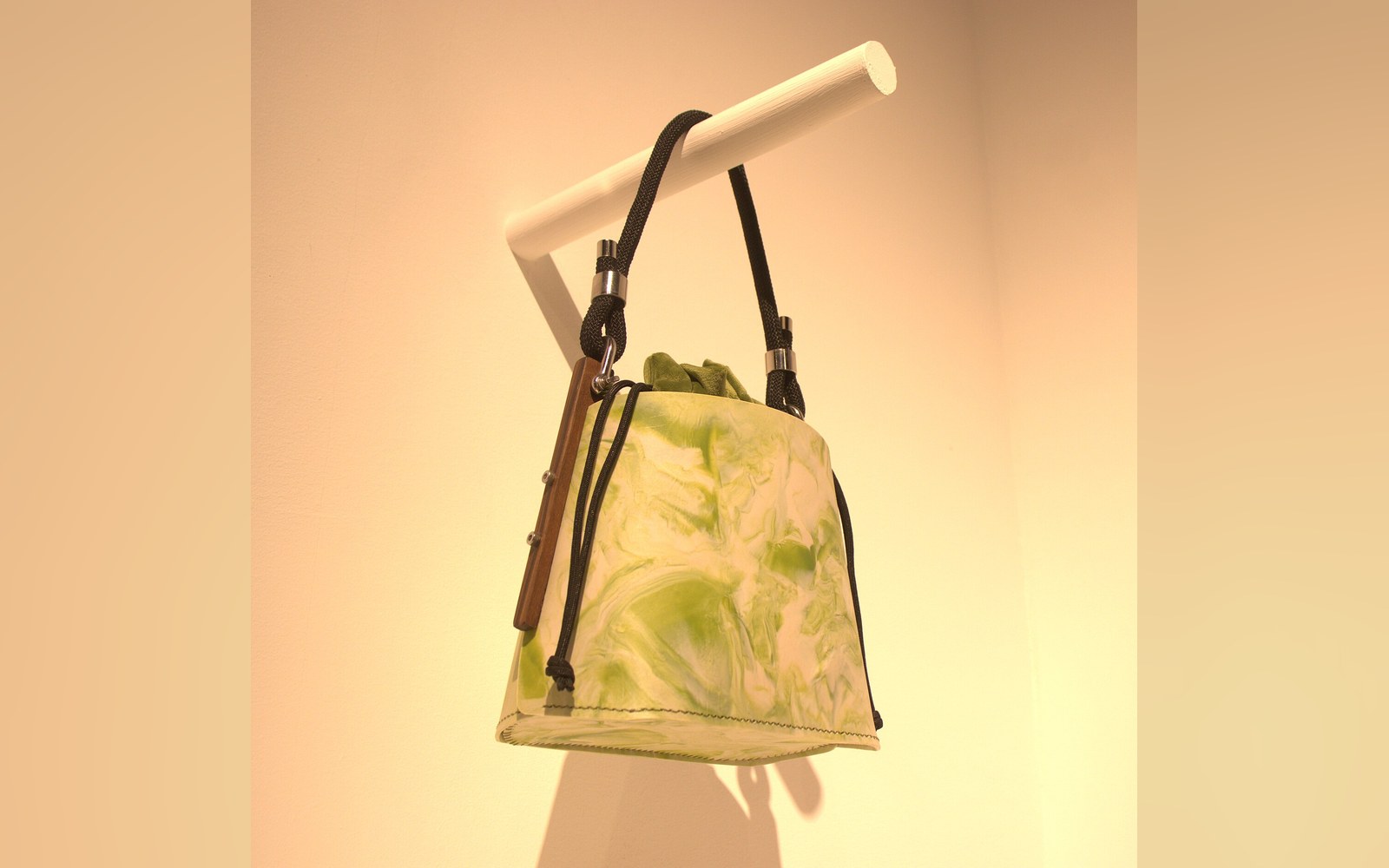 Marbled green and white handbag with cord straps hangs from a wall-mounted rod