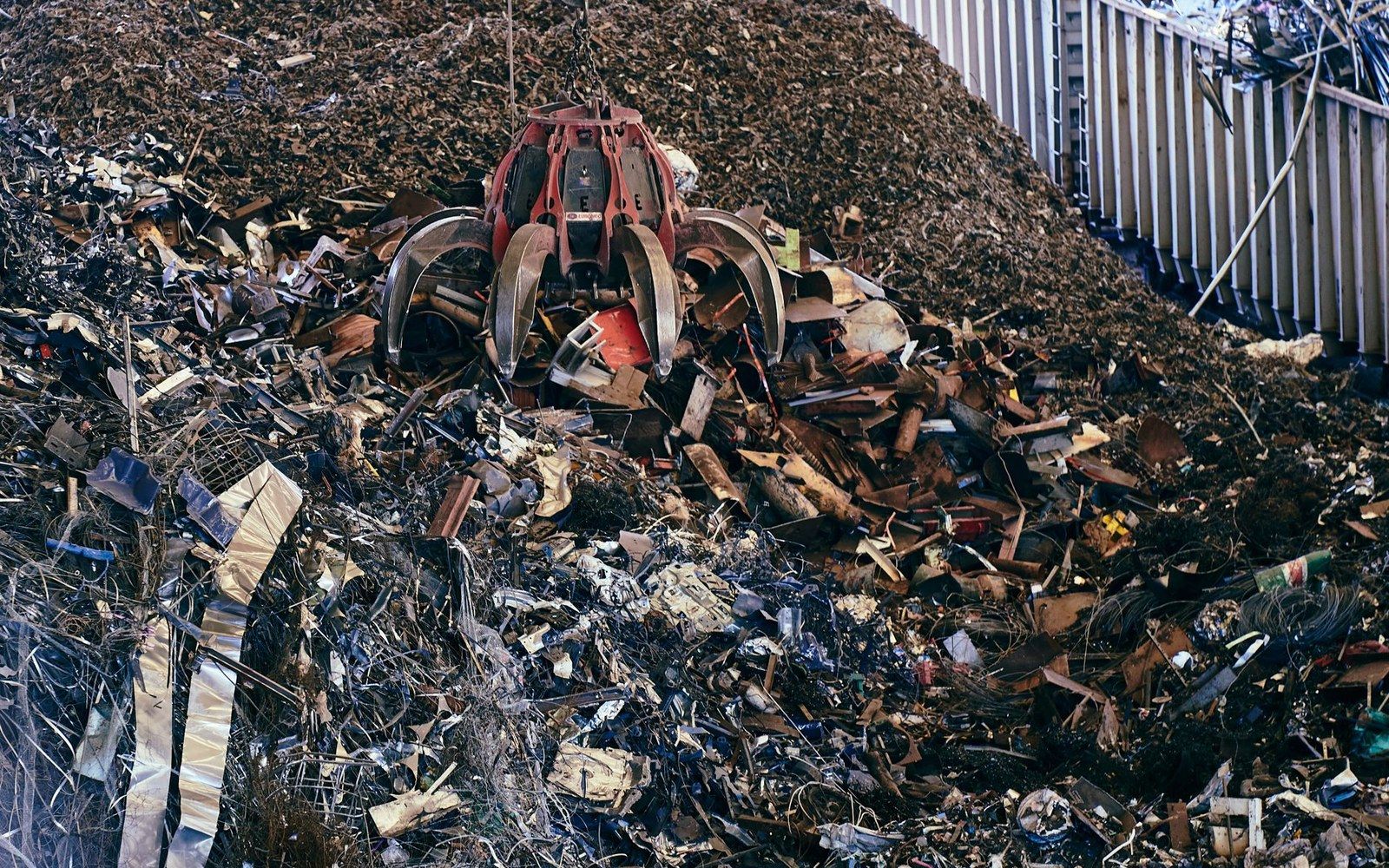 A mechanical claw grabs scrap metal from a large pile at a recycling yard