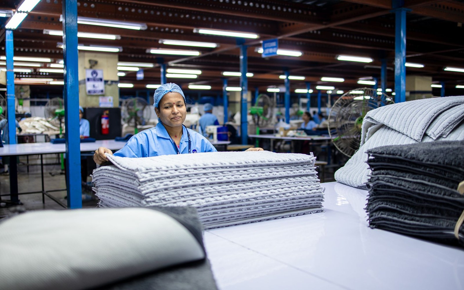 Workers sorting donated garments by hand at a moving belt in a textile-collection operator's sorting hall, bins of graded clothing visible behind them